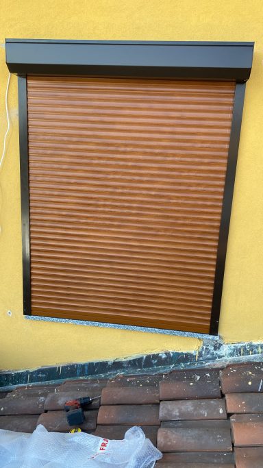 Tapparelle Rolled-up wooden blinds installed on a yellow wall with a tile roof below.